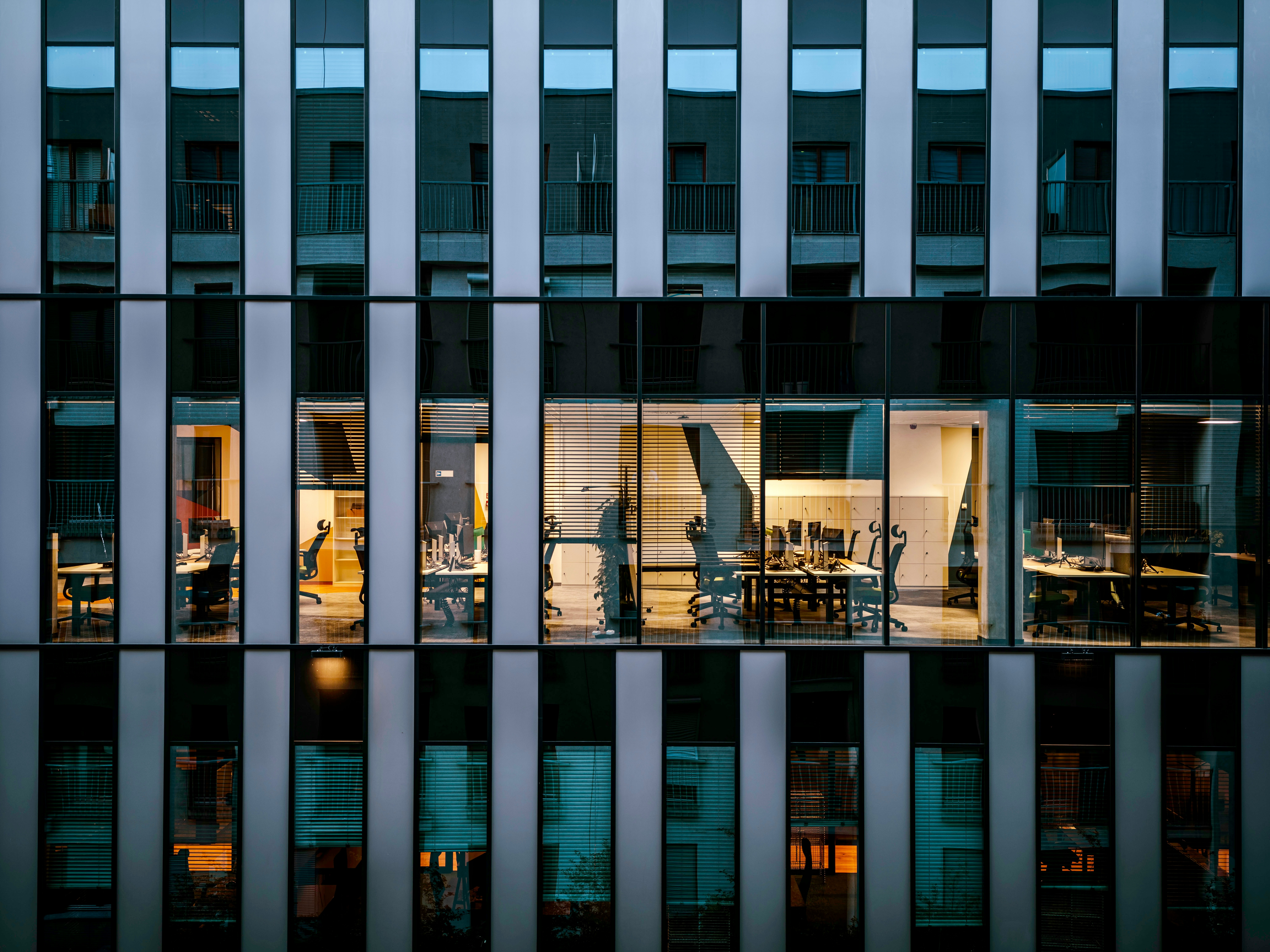 A tall glass building with an illuminated office inside